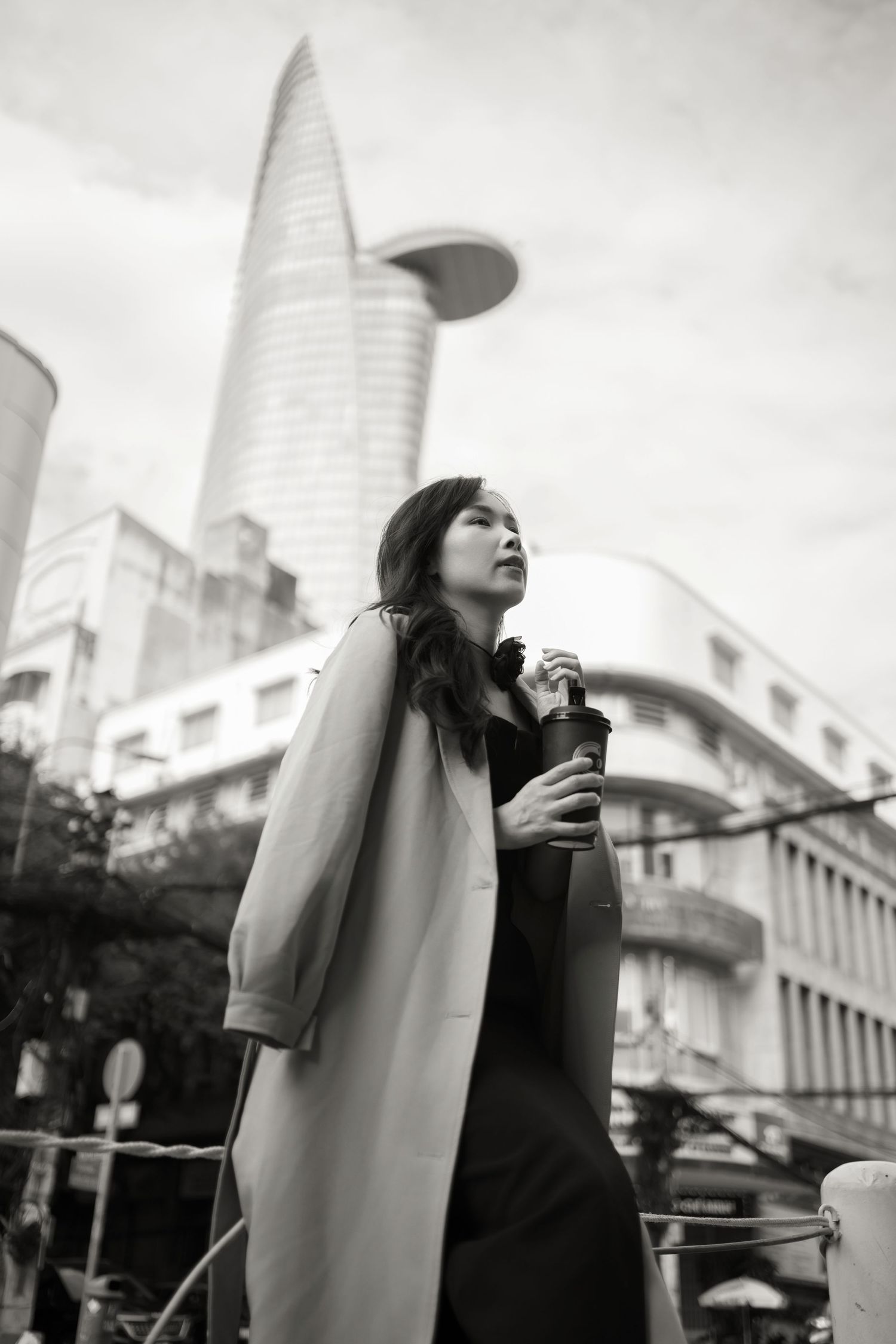 A black and white photo series shows a person holding a drink against an urban cityscape with modern buildings.