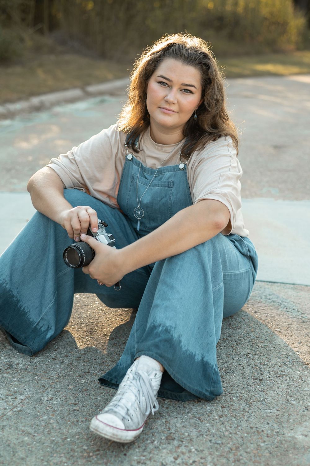 Casual portrait series showing someone sitting on pavement wearing denim overalls and white sneakers.