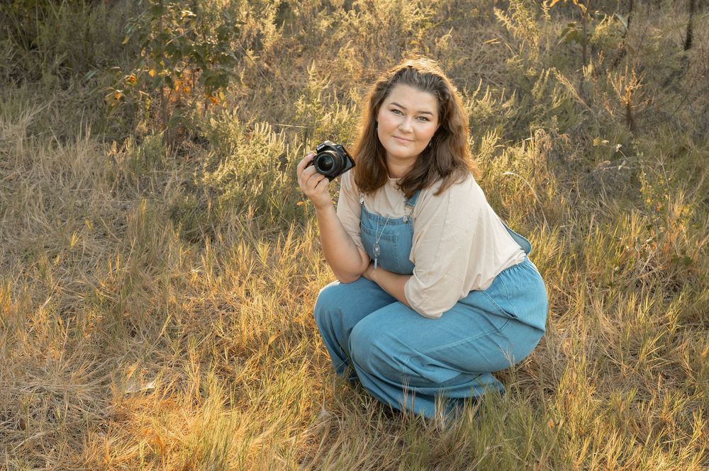 Photographer crouches in golden grass field at sunset holding professional camera.