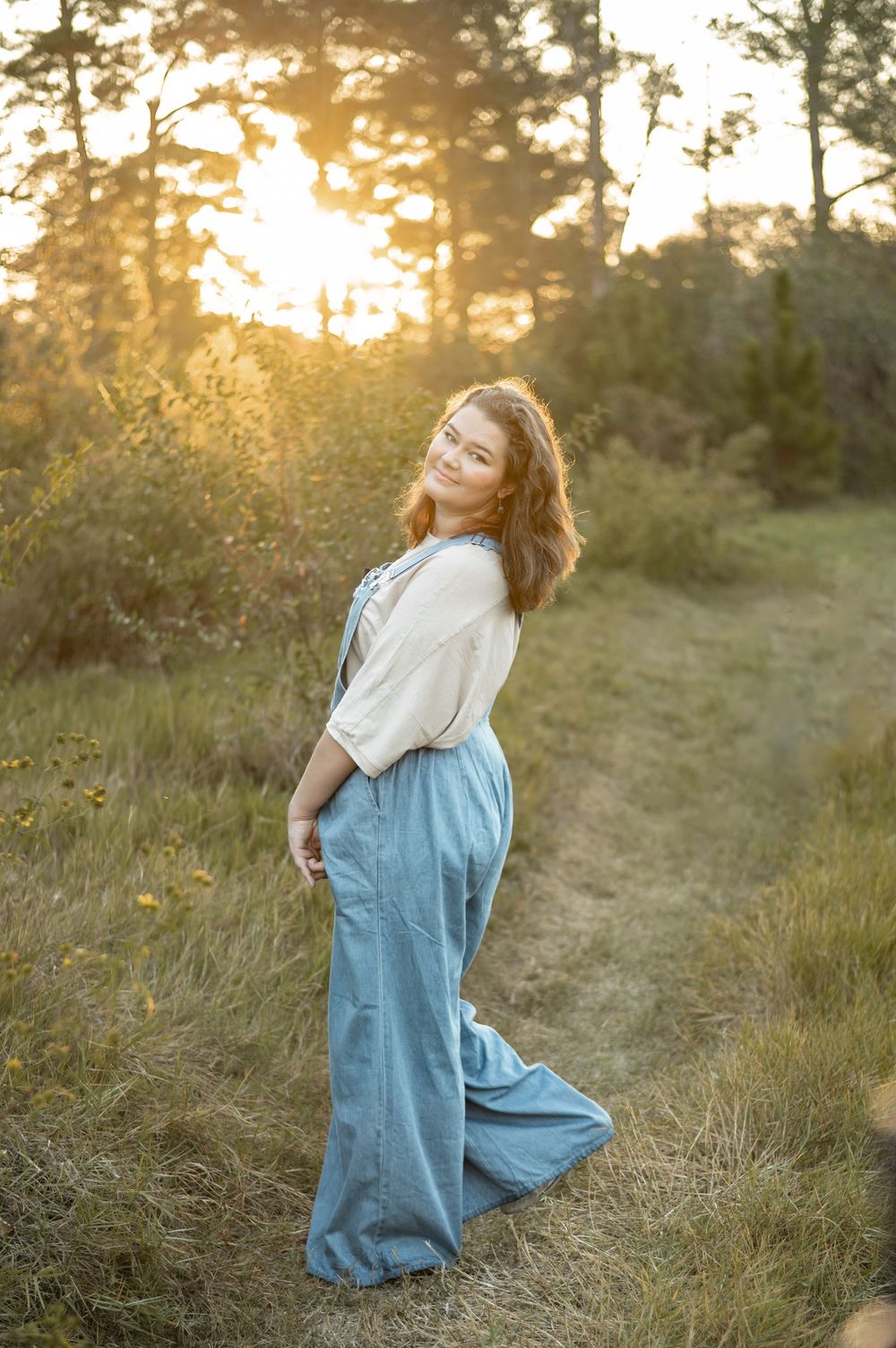 Dreamy outdoor photoshoot in a grassy field at golden hour featuring denim overalls and natural poses.