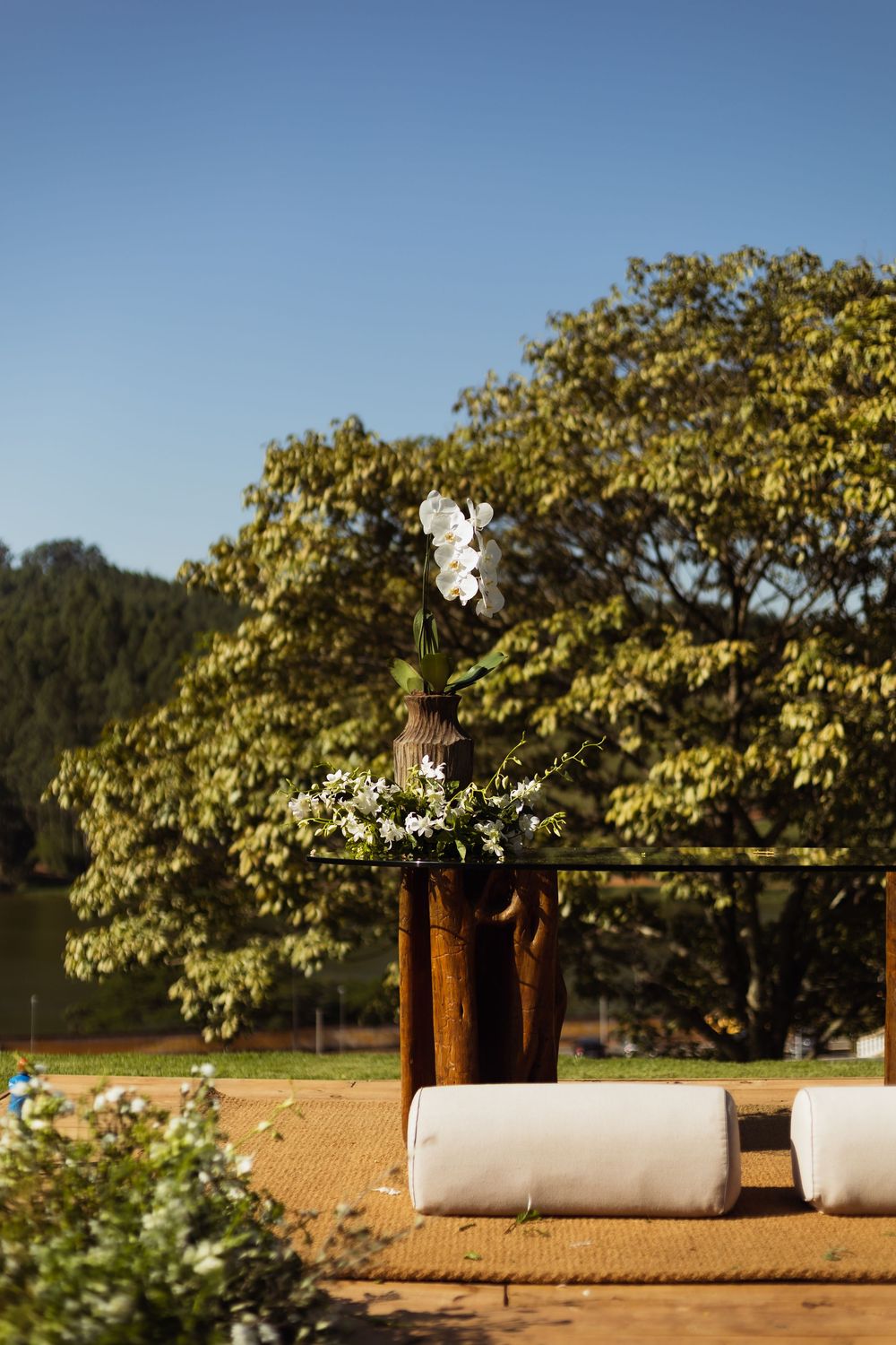 Rustic outdoor seating arrangement with white cushions and floral decorations against a sunny landscape.