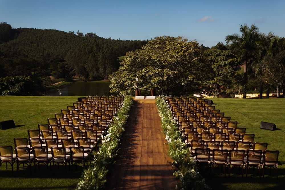 Rows of wooden chairs line a grassy outdoor ceremony space with palm trees and mountains in the background.
