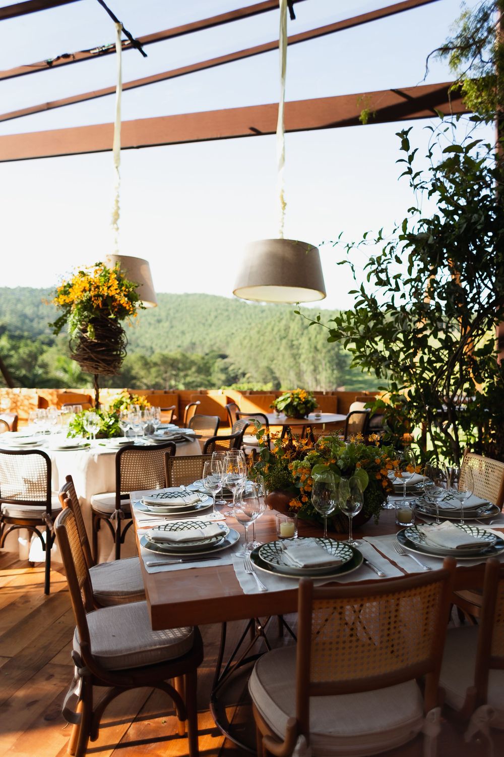 Elegant outdoor dining tables set with white linens and floral centerpieces under a covered patio with mountain views.