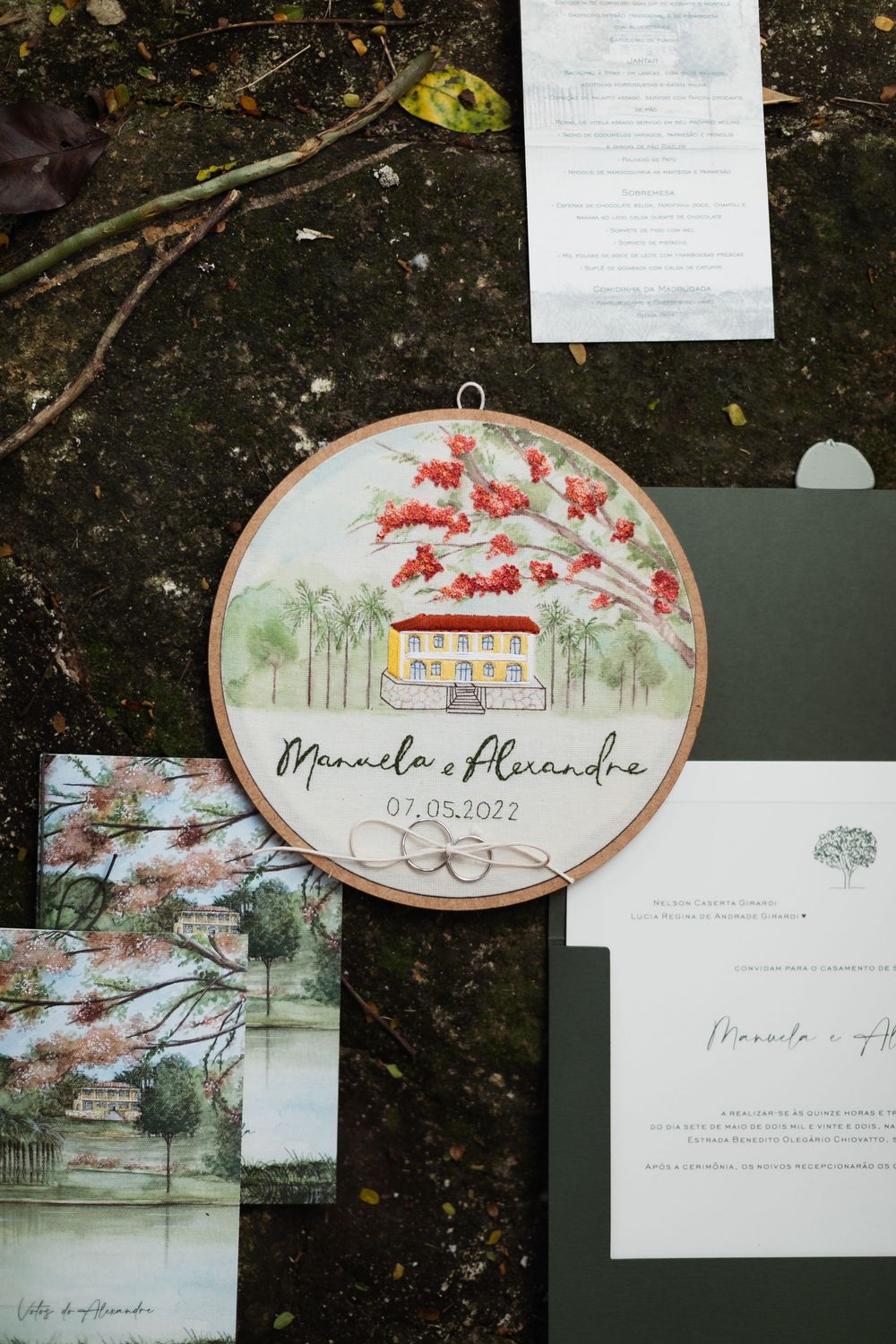 Artistic wedding invitations and embroidery hoops featuring delicate watercolor designs of houses and floral motifs.