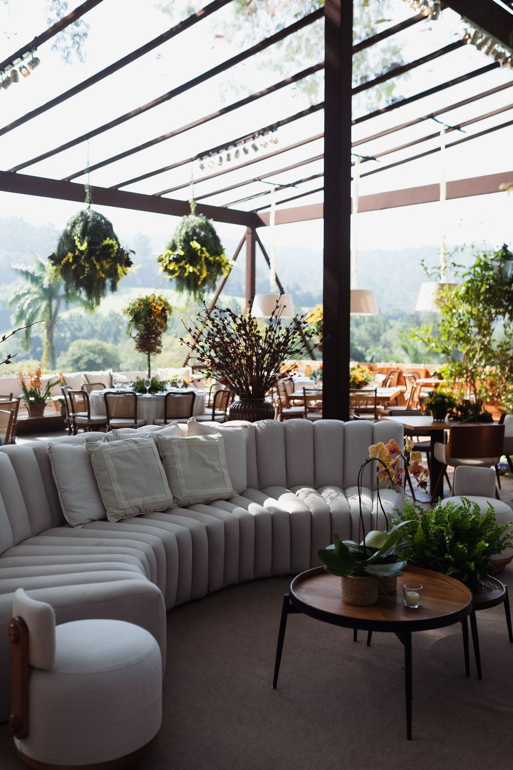 Modern lounge area with curved white sectional seating under a glass-covered pavilion with scenic views.