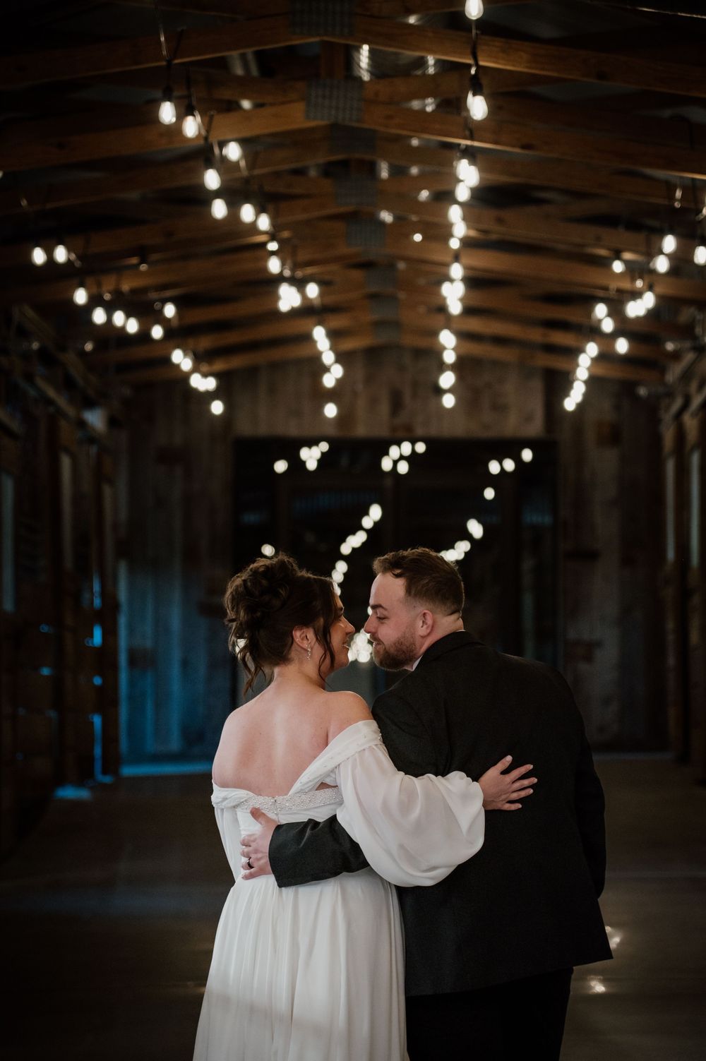 Romantic dance under string lights in a rustic indoor venue with exposed wooden beams.