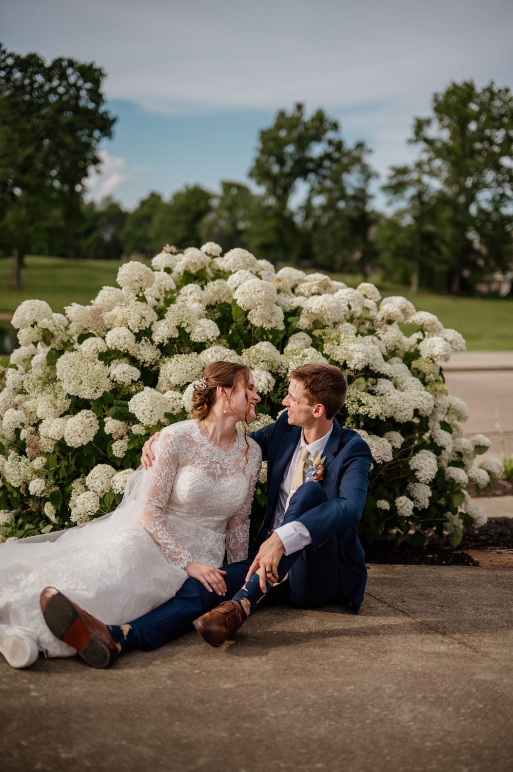 Wedding couple relaxing by blooming white hydrangea bushes outdoors.