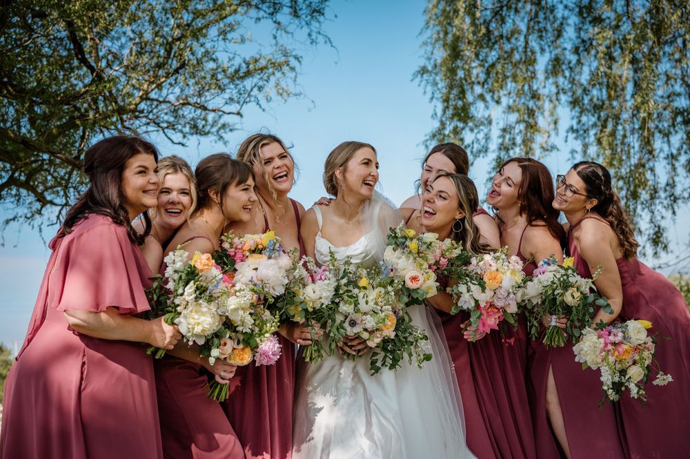 Wedding party in burgundy dresses posing outdoors with floral bouquets.