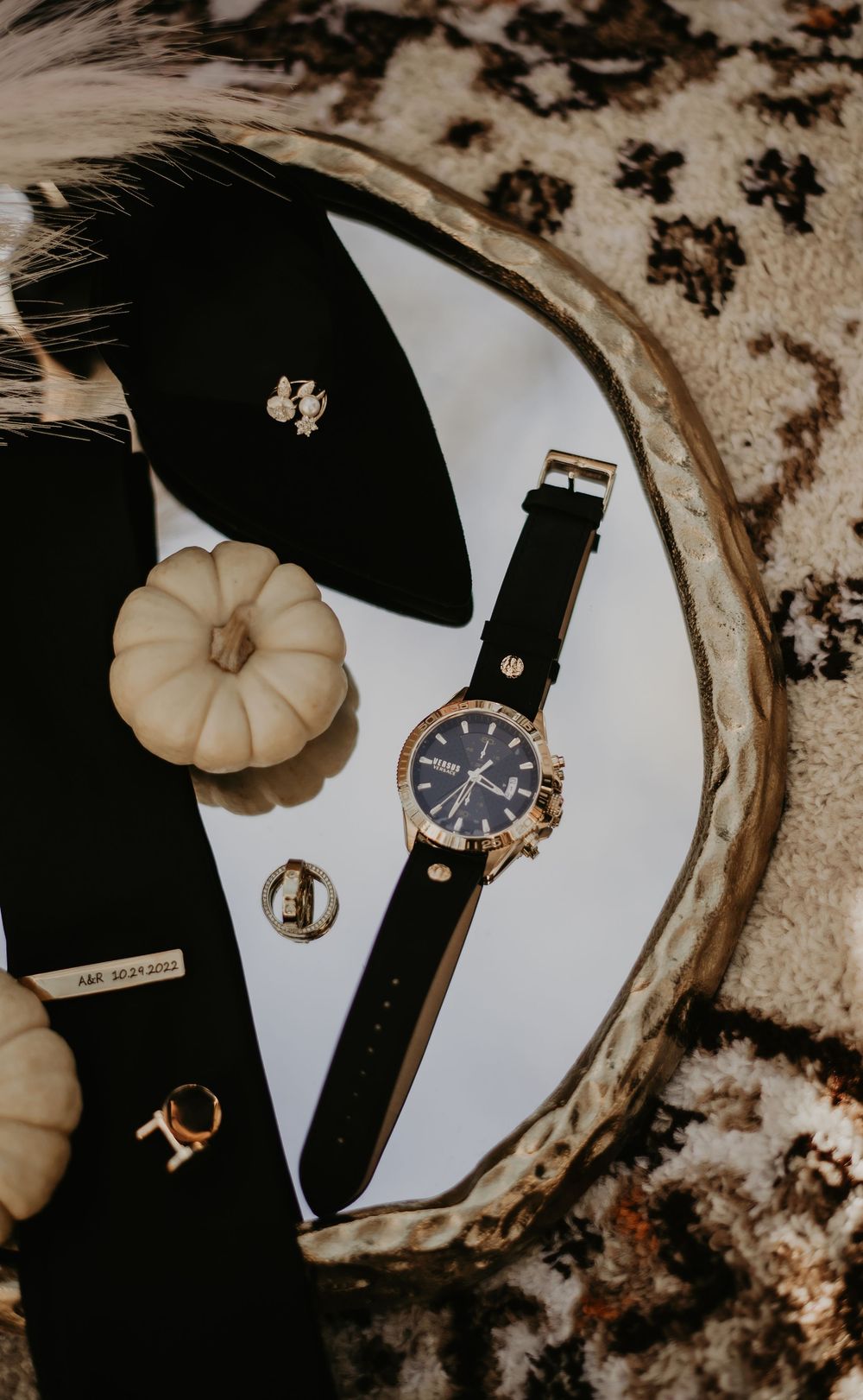 Elegant wristwatch and small decorative pumpkins arranged on a contrasting dark and light surface.