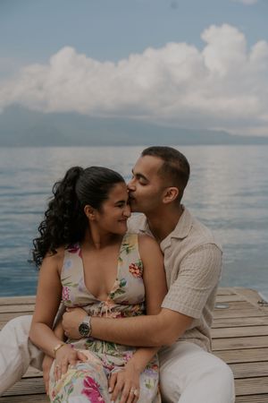 A couple shares intimate moments on a wooden dock overlooking a serene ocean under cloudy skies.
