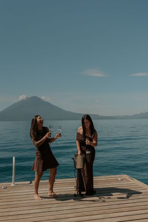 Two people share a romantic moment on a wooden dock overlooking a serene lake with mountains in the background.