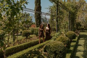 People explore a lush garden pathway with green hedges and trees on a sunny autumn day.