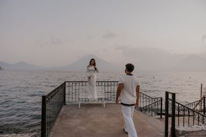 Couple in white outfits on a lakeside pier with mountain views at dusk.