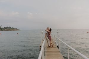 Romantic couple kissing on a white pier overlooking a calm ocean on a cloudy day.