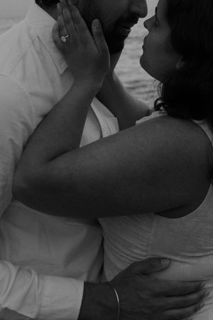 Black and white photo of a couple embracing and gazing at each other, woman wearing an engagement ring.