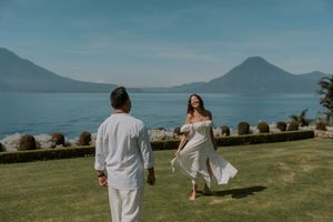 Couple in white attire having a romantic moment by a scenic lake surrounded by mountains.