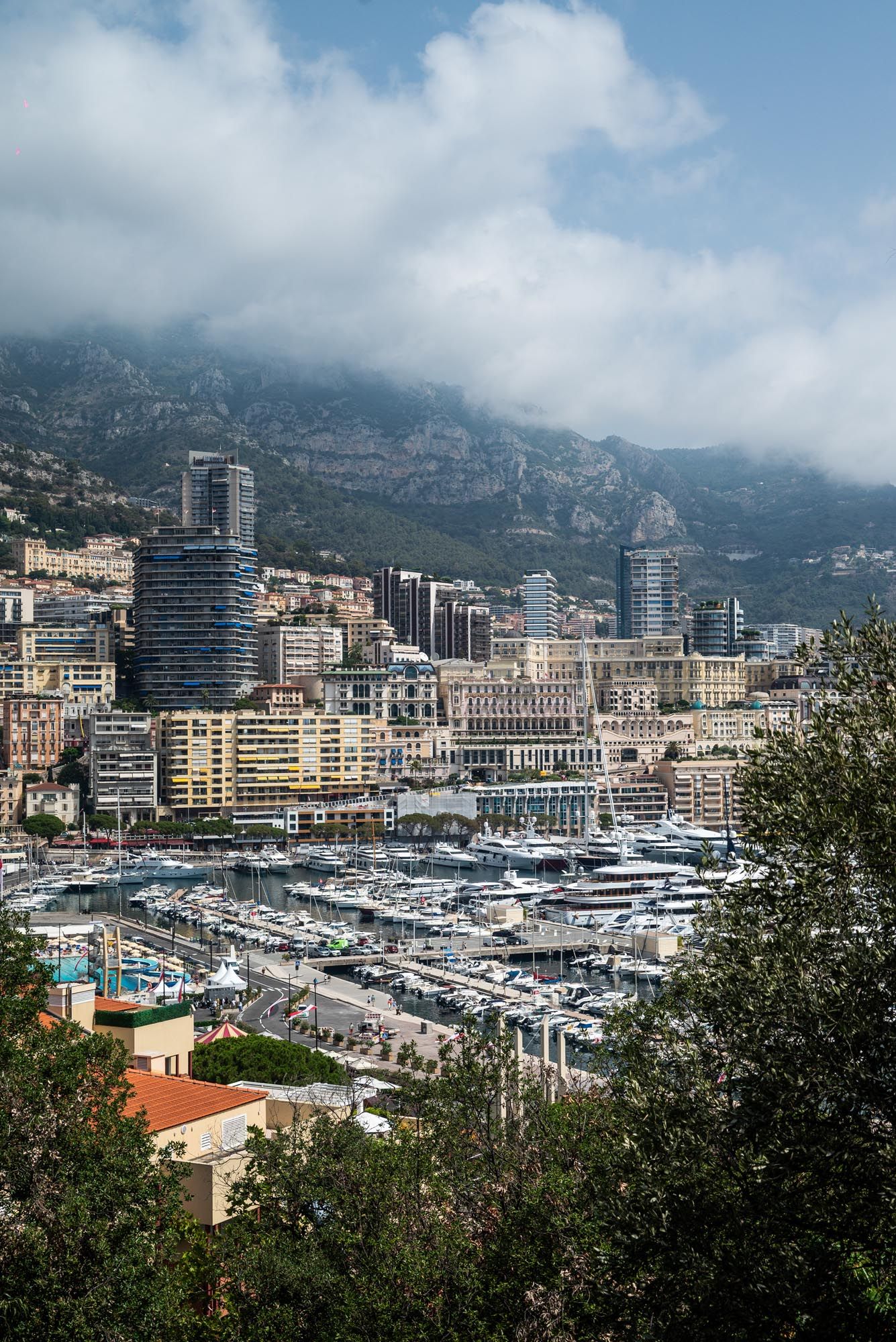 Luxury yachts and boats fill the marina of Monte Carlo, Monaco with high-rise buildings and mountains in the background.