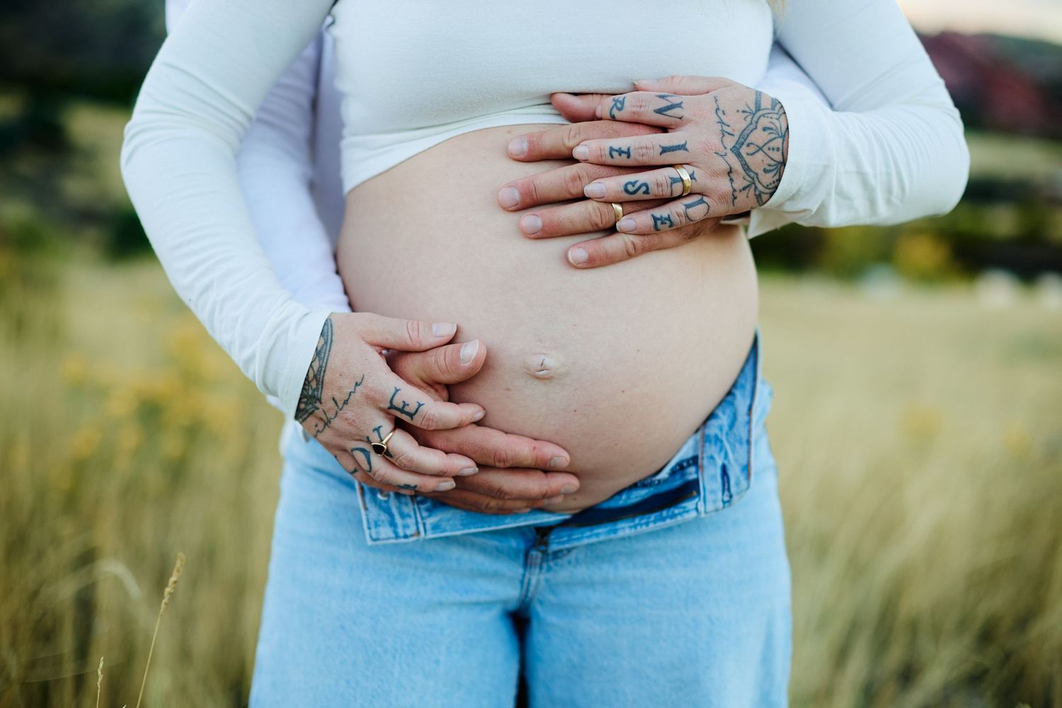 Close-up shots of hands cradling a pregnant belly in blue jeans and white top against a natural outdoor background.