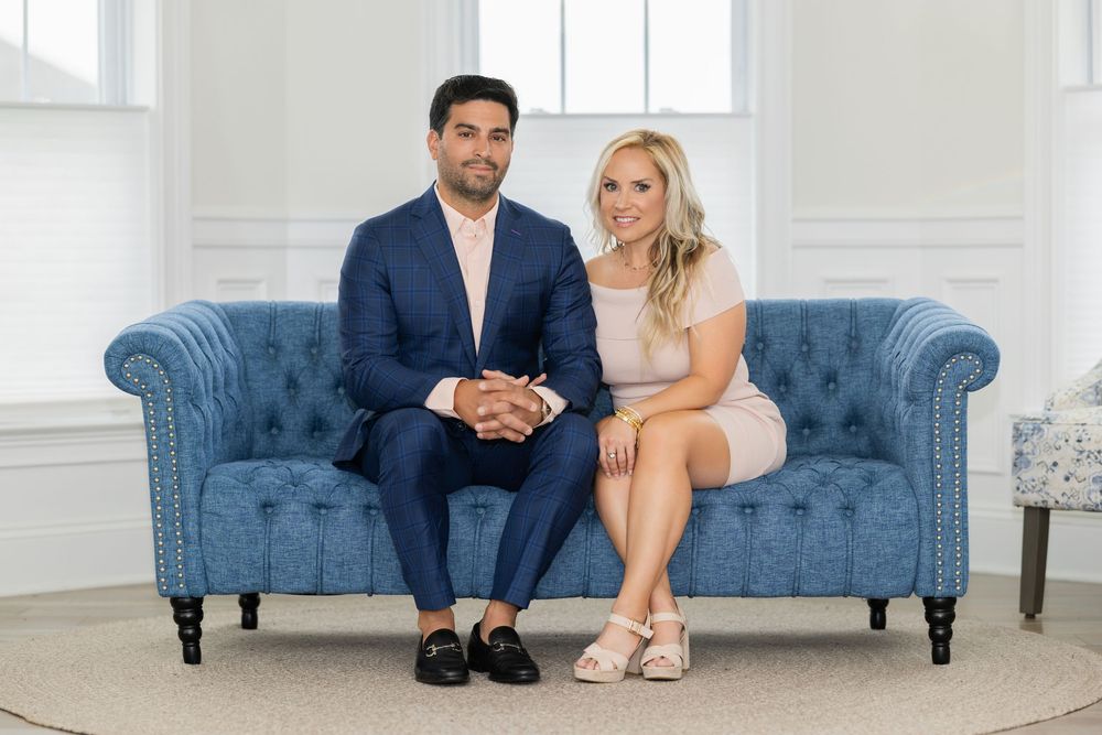 Couple lounges together on blue couch during indoor photoshoot.