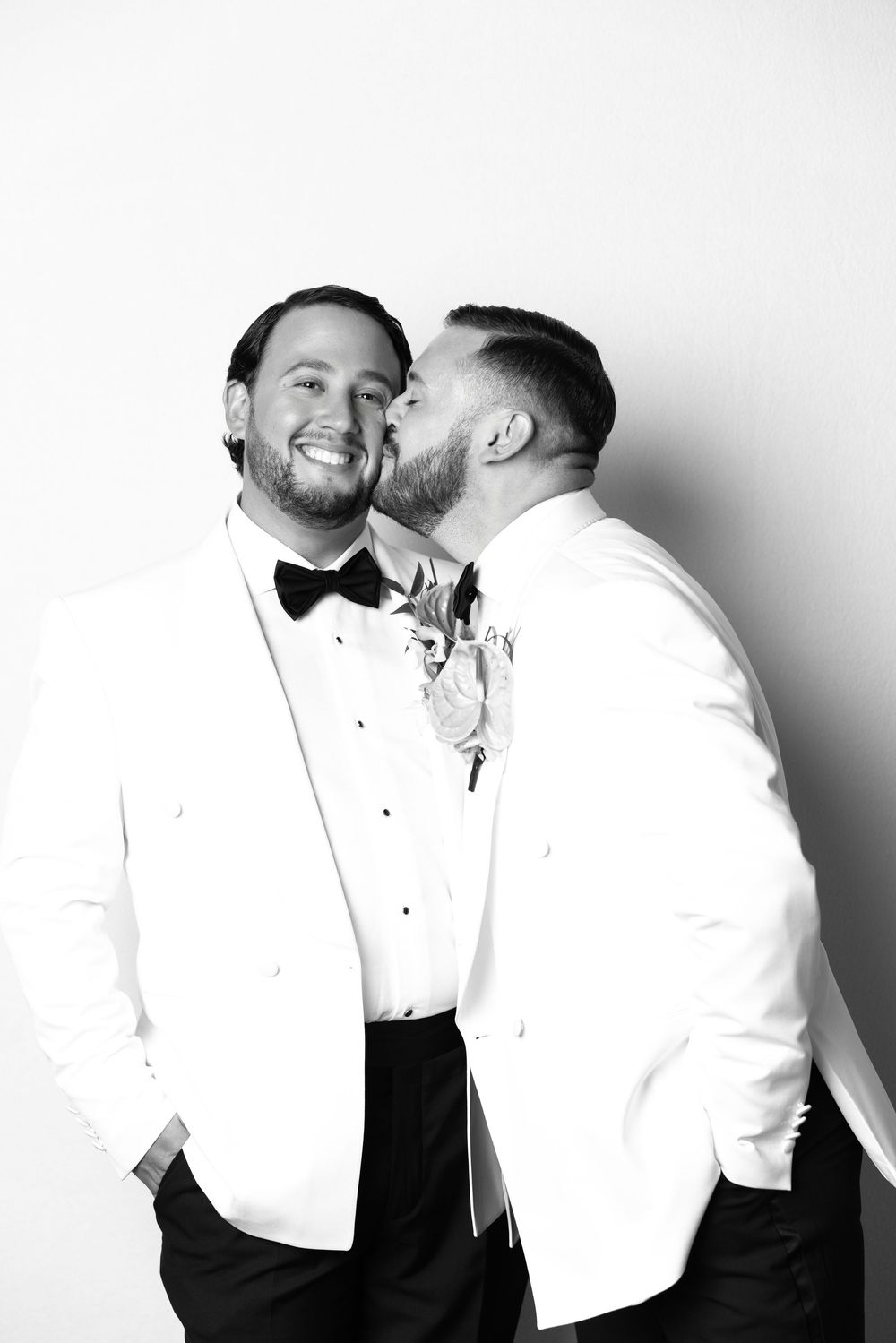 A black and white photo of two people in formal wear sharing an affectionate moment.