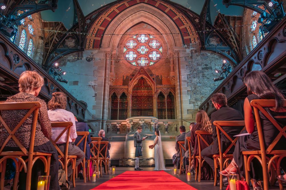 Gothic church interior with red carpet aisle, wooden beams, and stained glass windows illuminated in dramatic lighting. Cottiers