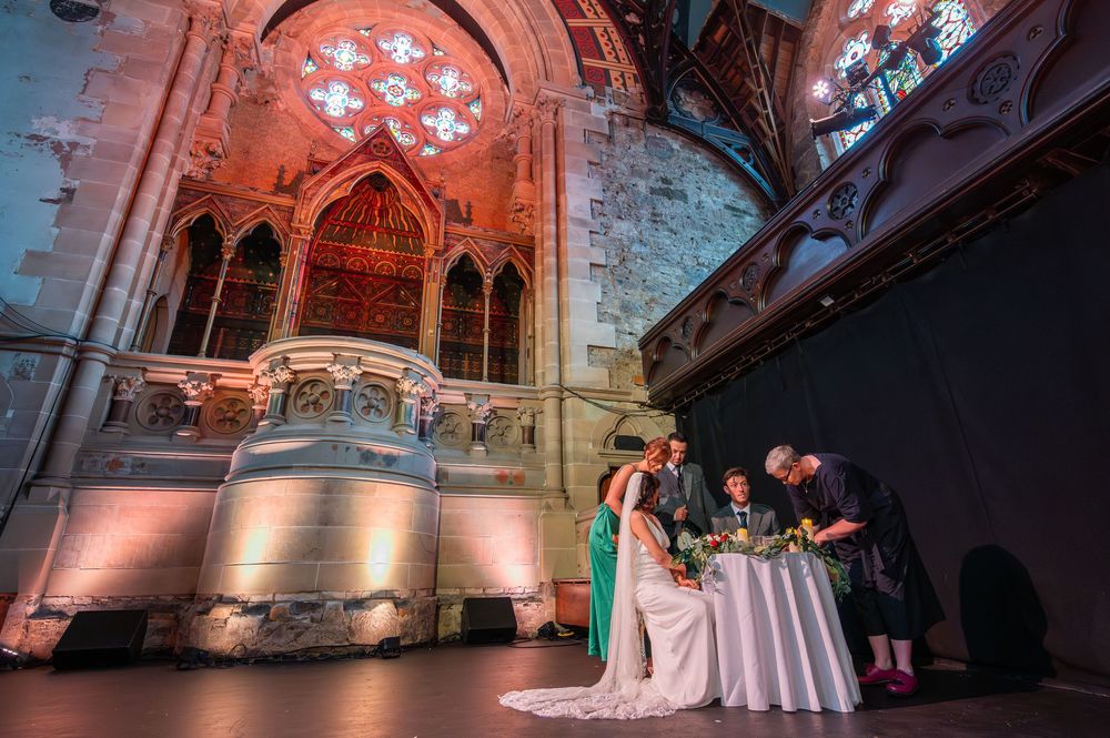 Elegant wedding reception setup in a historic stone church with dramatic architectural lighting and vaulted ceilings. Cottiers