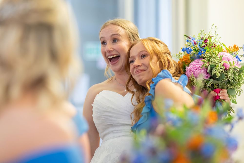A group of people celebrate joyfully at an event with colorful floral decorations in the background.