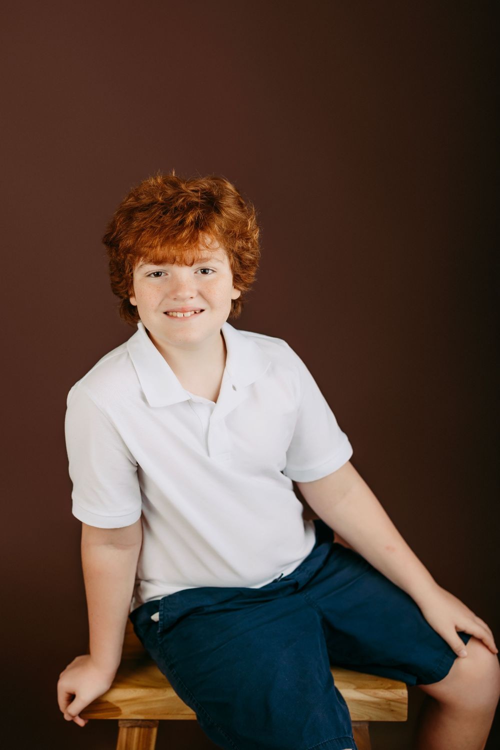 Child in school uniform sitting casually on wooden bench during professional photo session.