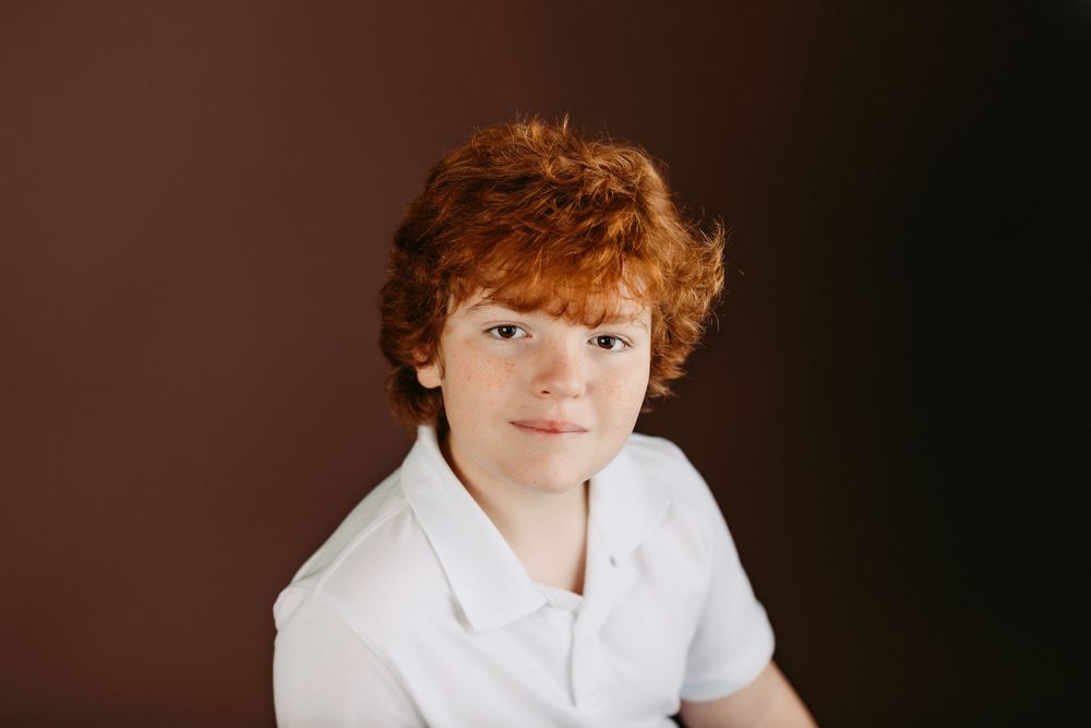 Studio photograph of a child in white collared shirt against dark brown backdrop.