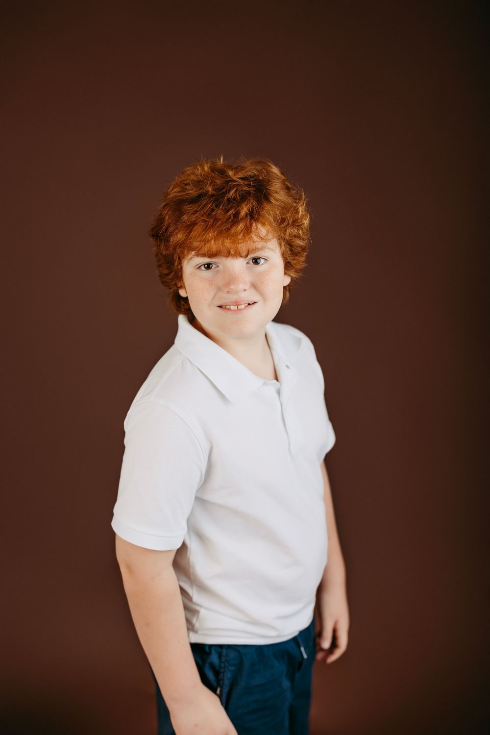 Portrait against brown background showing person in white polo shirt standing casually.
