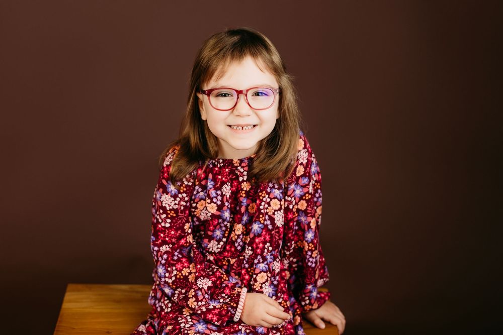 Young person wearing glasses and floral print dress poses during professional photo session.
