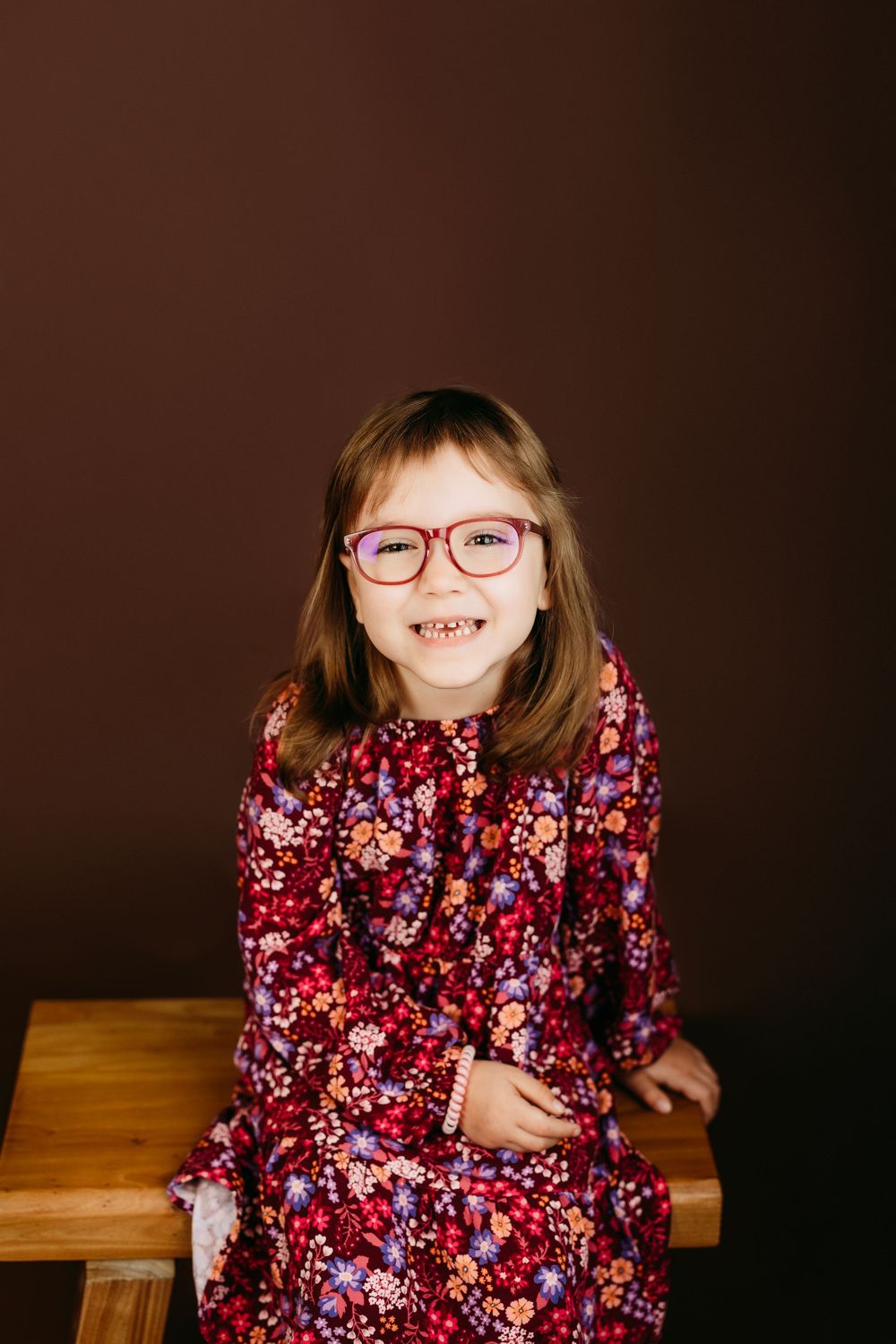 A series of photos showing a child in a floral print dress sitting on a wooden surface against a dark background.