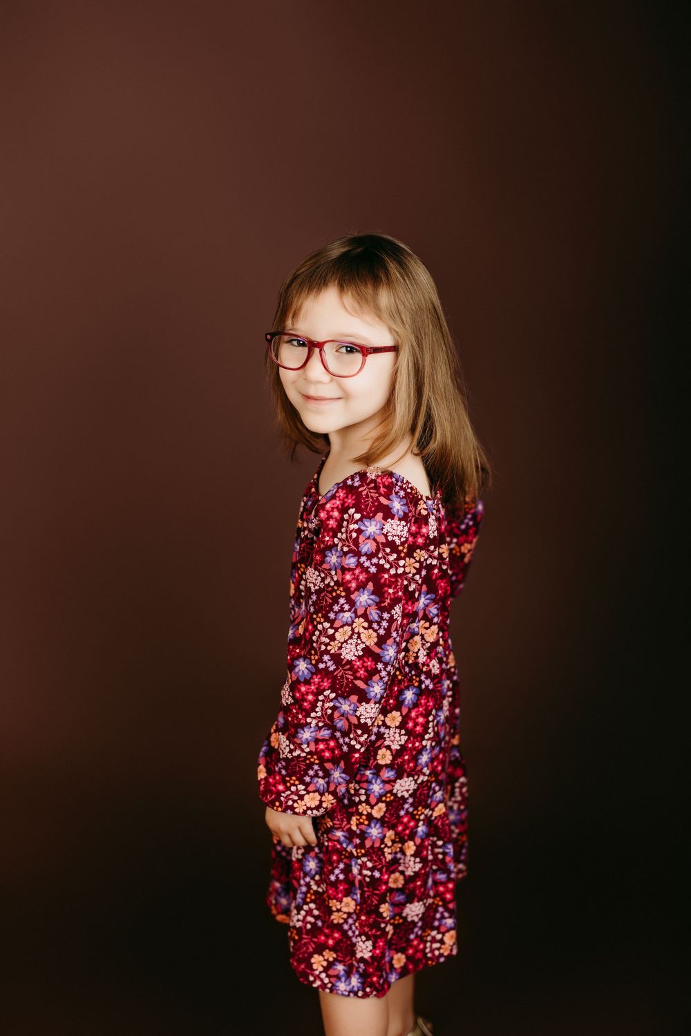 A floral burgundy dress with long sleeves against a dark brown studio backdrop.