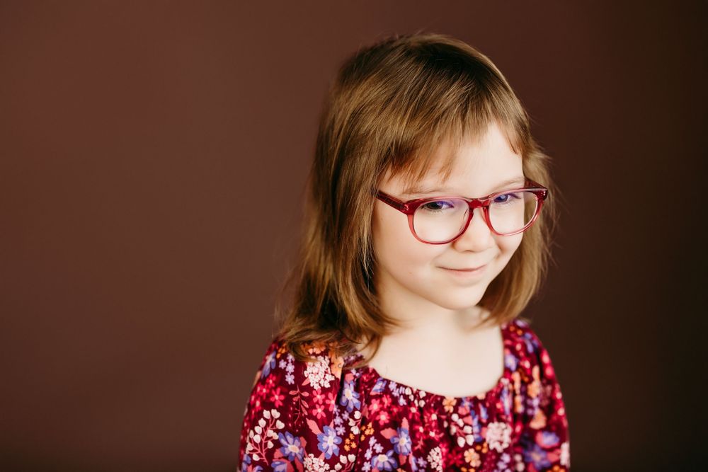 Side profile portrait of person wearing glasses and floral dress against brown backdrop.