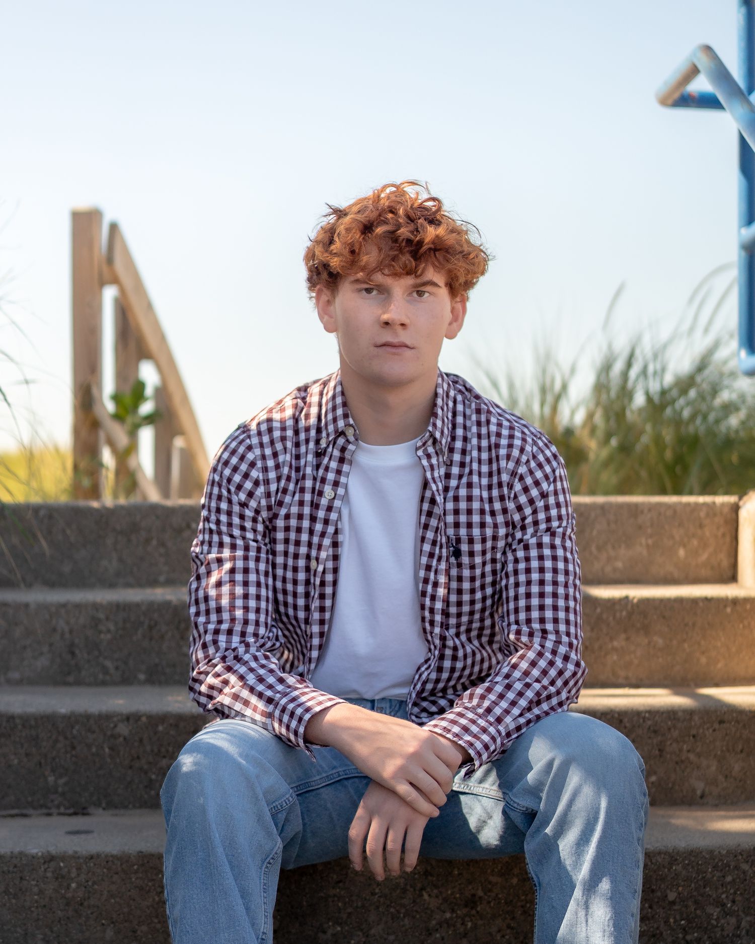 Casual outdoor portrait featuring plaid shirt and jeans on concrete steps.