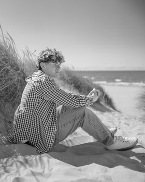 A series of black and white photos showing someone reclining on sand dunes wearing checkered clothing.
