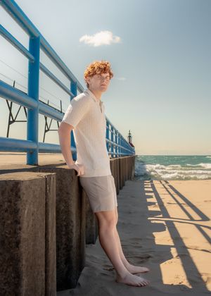 Person in light clothing sitting on concrete blocks along a beachfront pier.