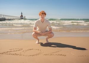 Panoramic beach scene with someone sitting near a pier and waves rolling in.