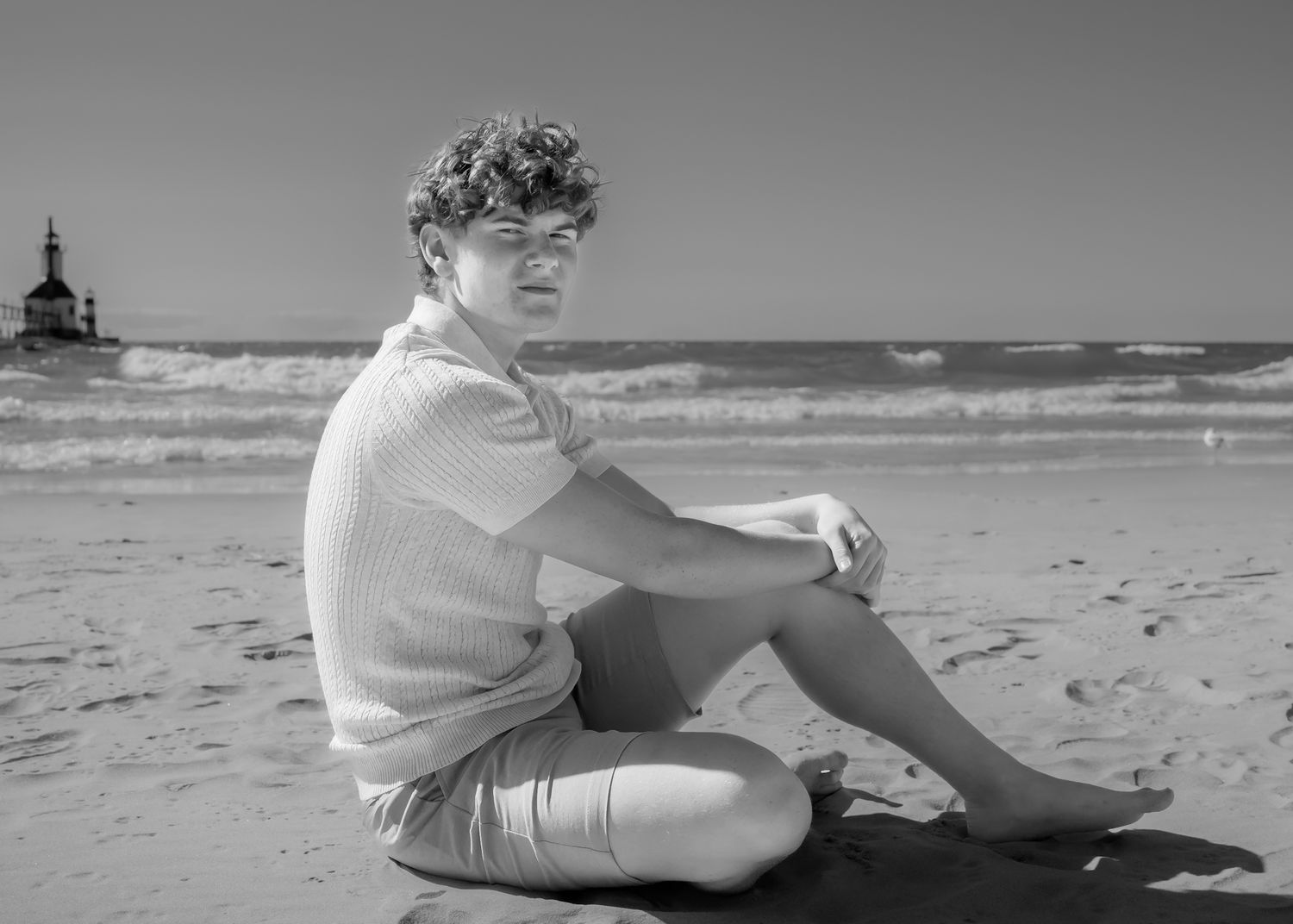 Black and white photos of someone sitting on a beach near the water.