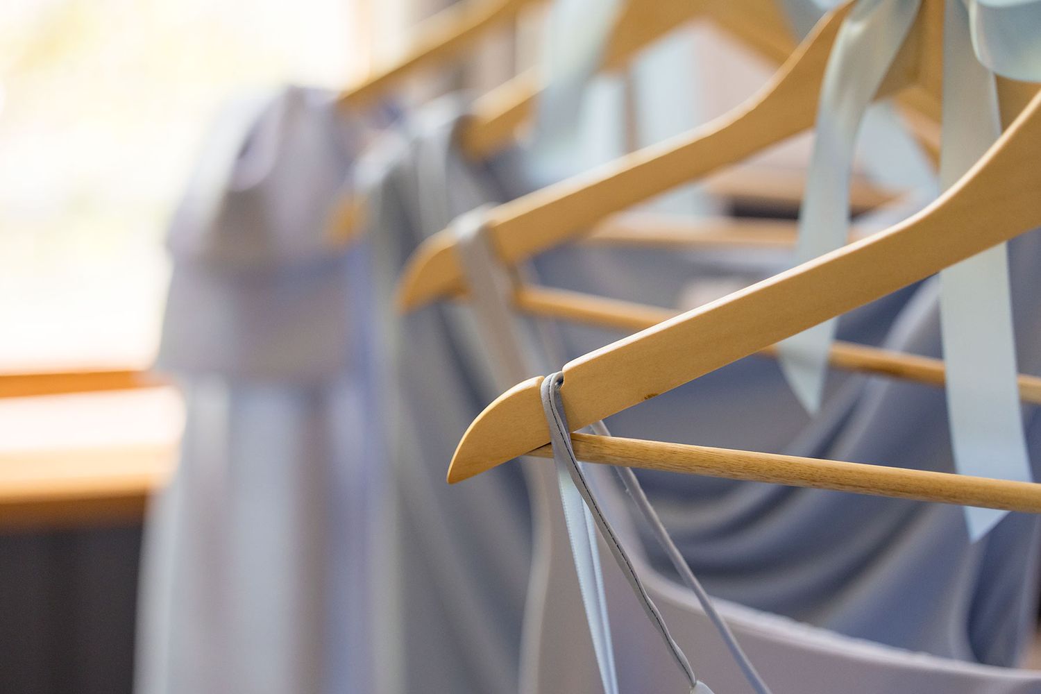 A row of wooden coat hangers on a clothing rack with gray garments hanging in the background.
