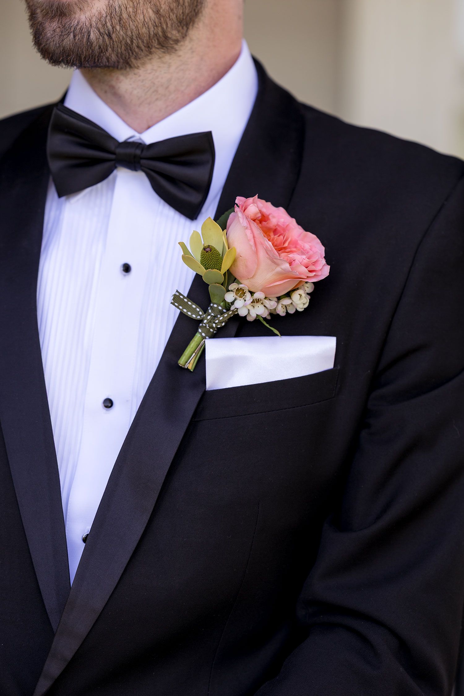 Close-up of black tuxedo with bow tie and pink rose boutonniere on lapel with white pocket square.
