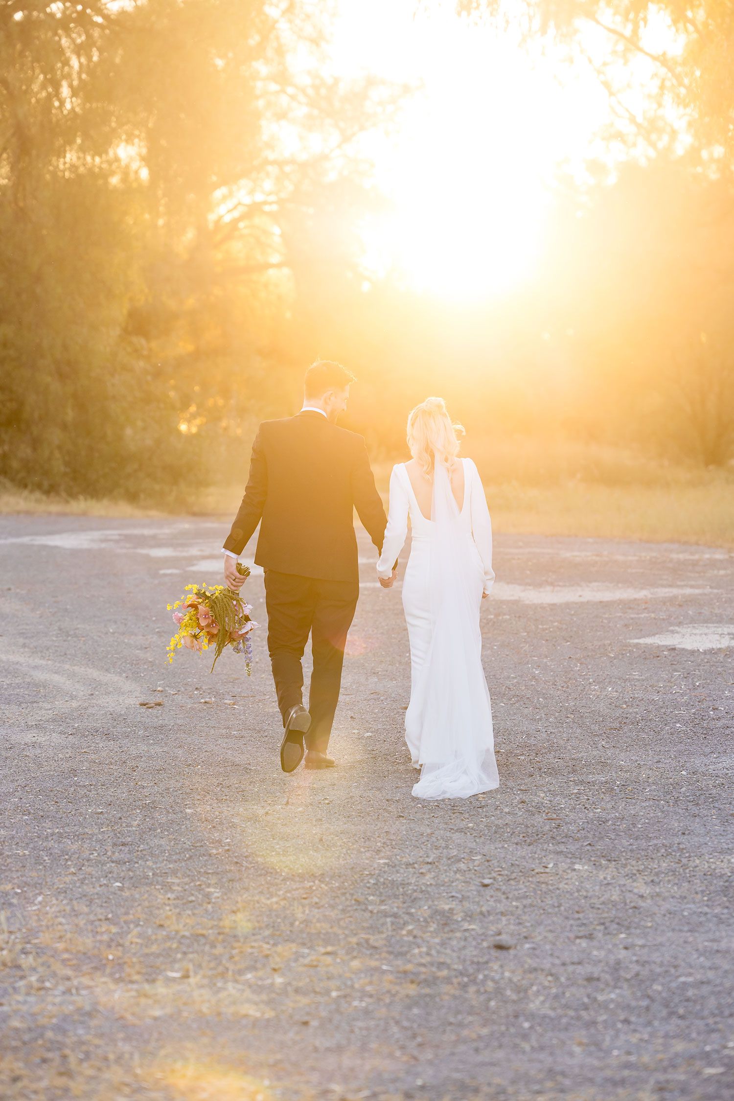 A couple walking hand in hand during golden hour sunset casting long shadows on a gravel path.