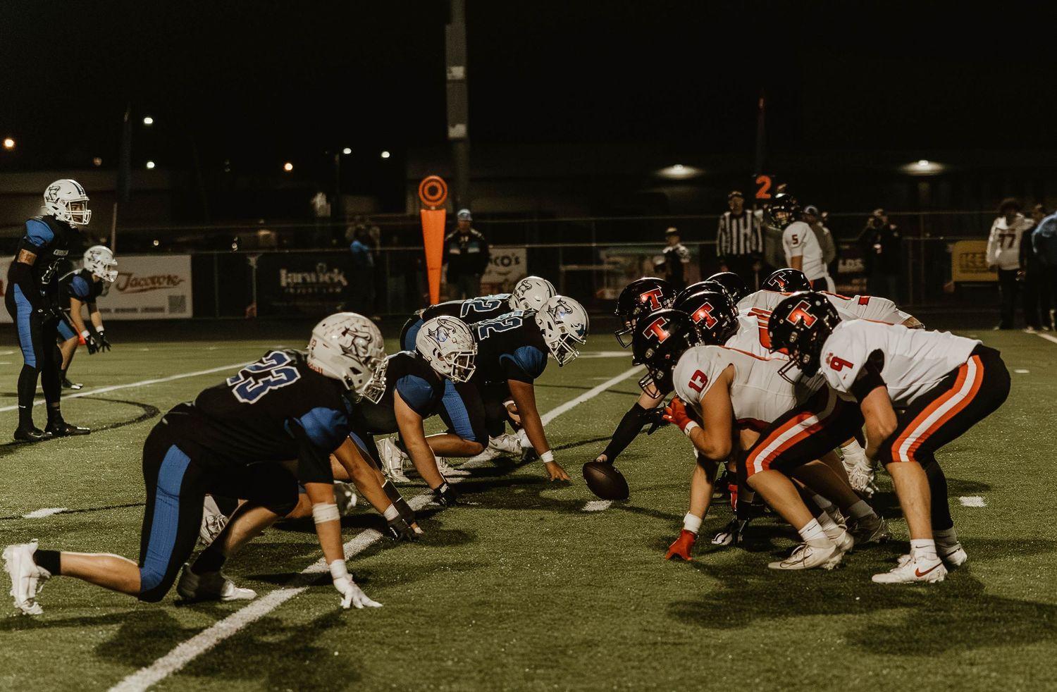 Football players line up in formation on a grass field during a nighttime game under bright stadium lights.