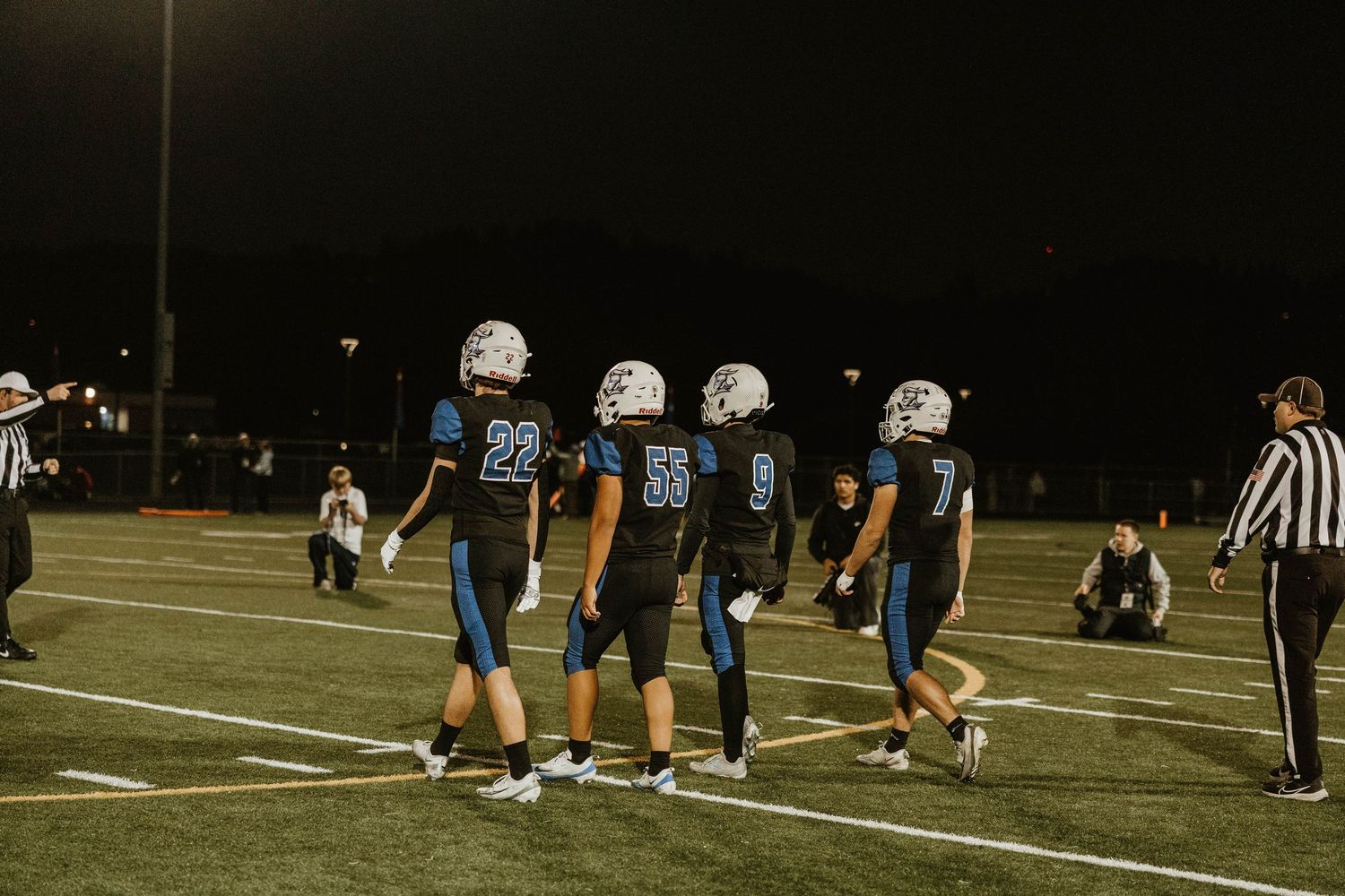 Wide view of football players and officials spread across a dark field during a nighttime game.