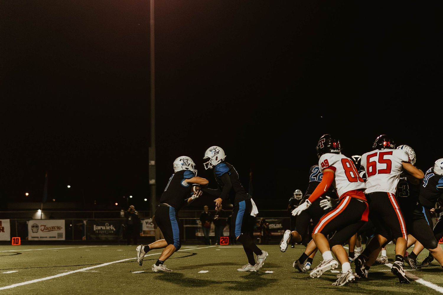 Football players line up at the line of scrimmage during a nighttime game under stadium lights.