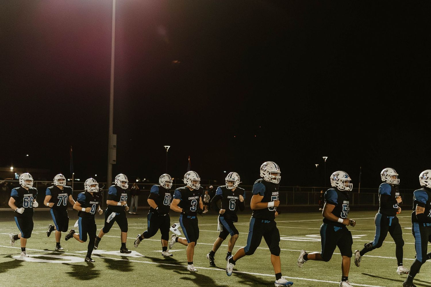 Football players line up in formation on a dark field during a nighttime game under bright stadium lights.