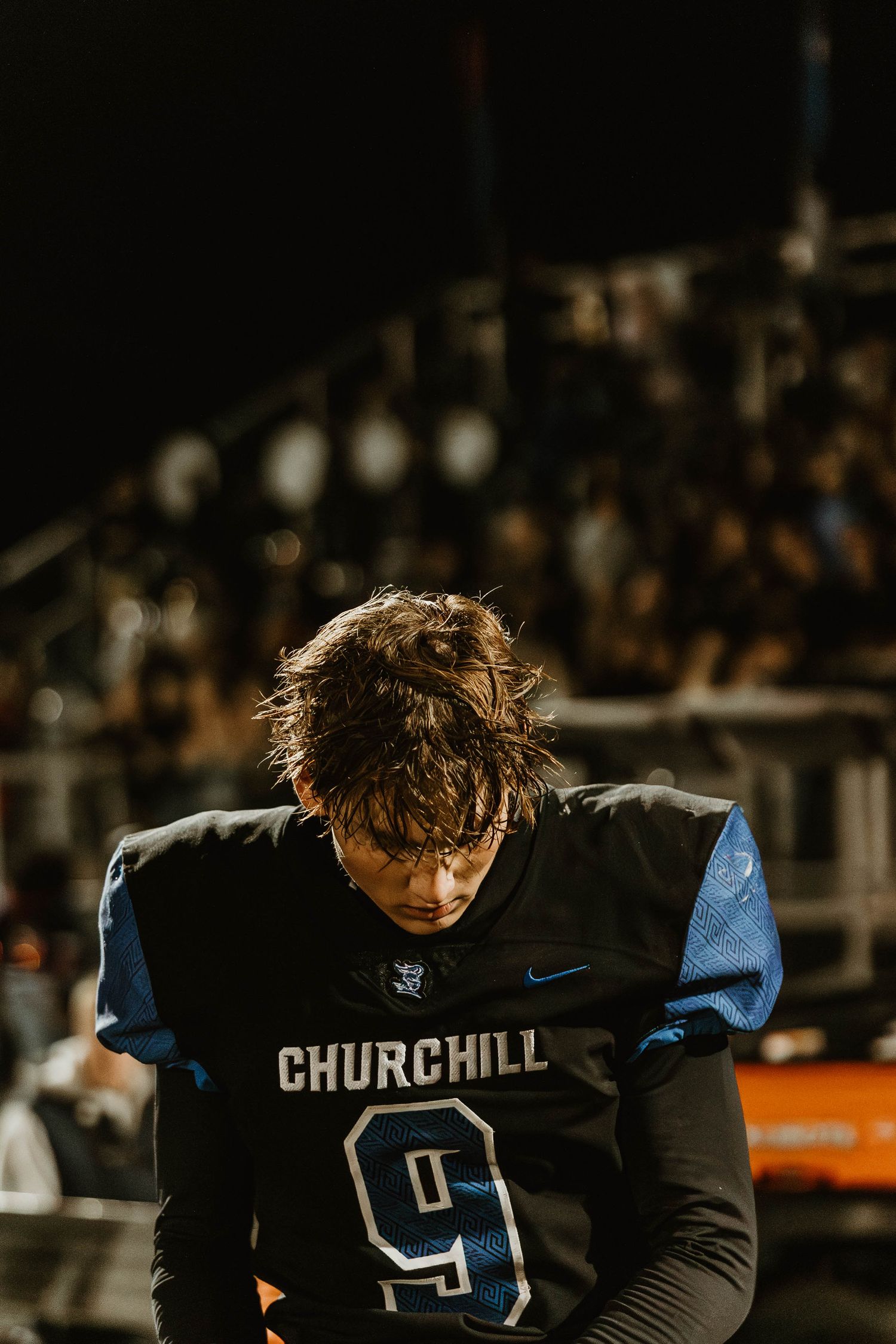 Football players in Churchill team uniforms huddle on the field during a night game.