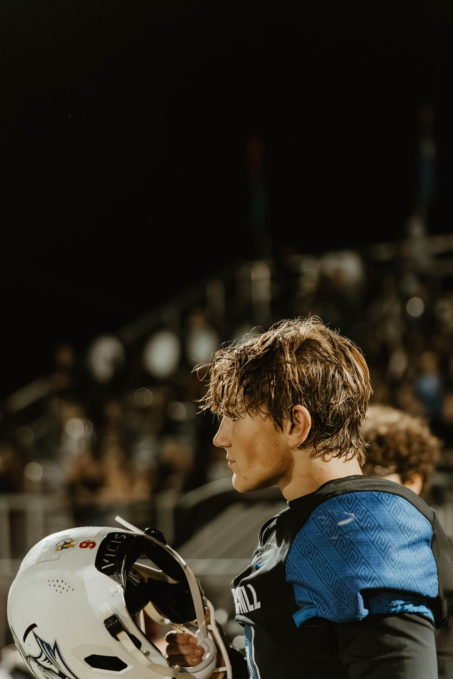 Athletes in blue jerseys and white helmets stand together on a sports field during a nighttime game.