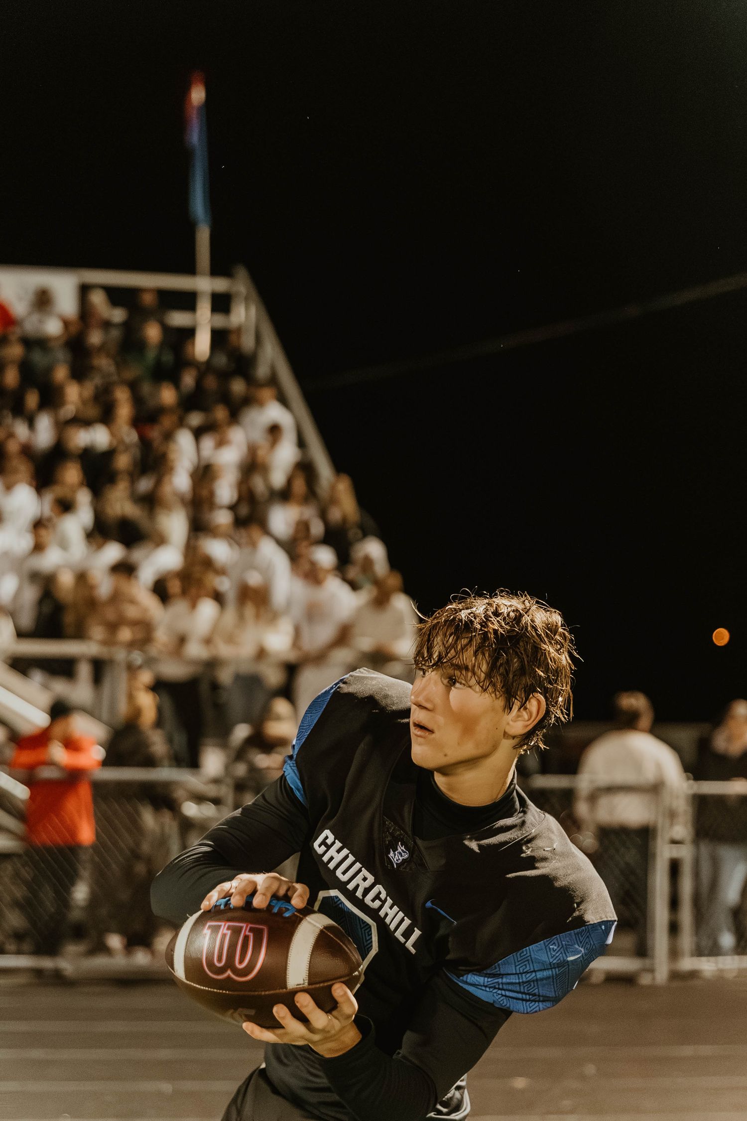 Football player in black uniform runs with ball during nighttime game with crowd in background.