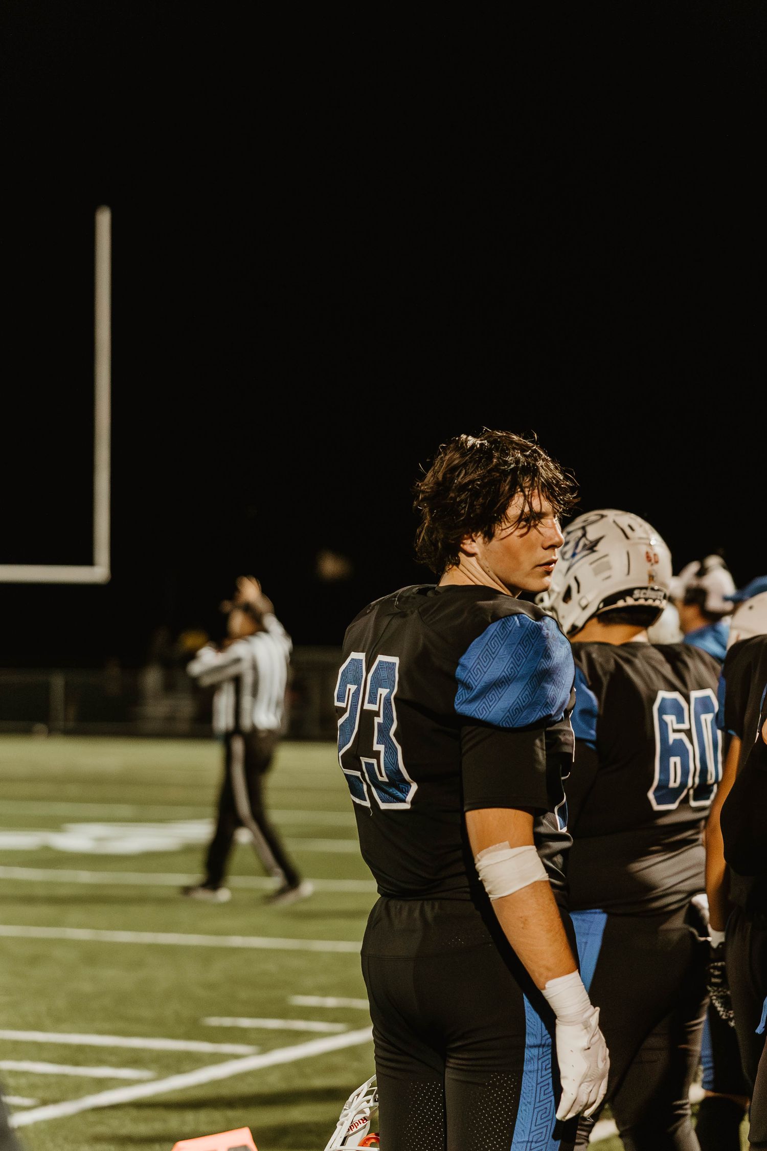 Football team members in black and blue jerseys stand together on the field at night.